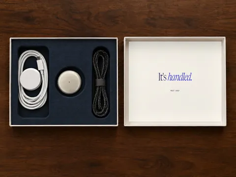 The open box: dock, pendant and cord in navy foam, lid reading It’s handled.